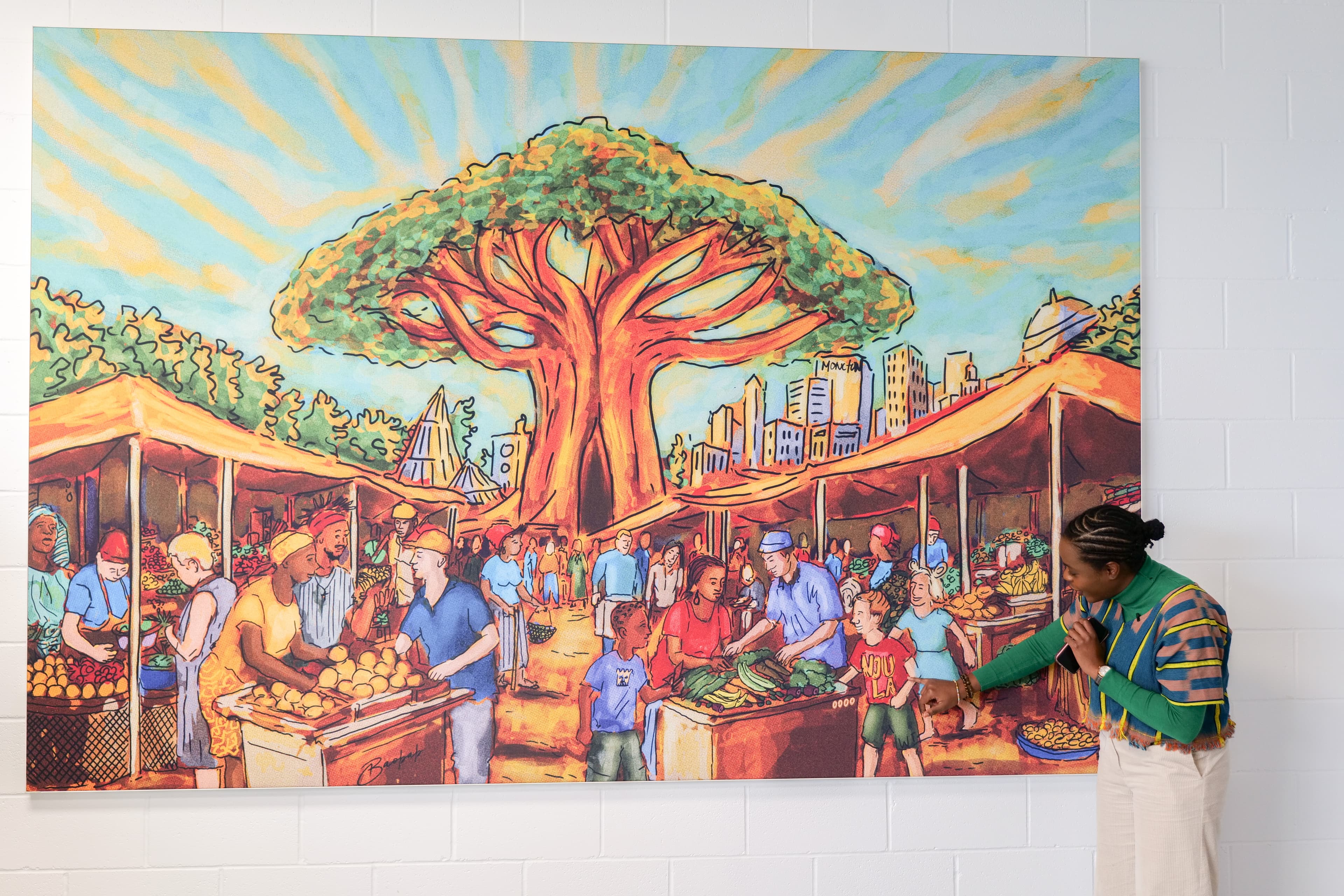Esther Ibang, fondatrice de ComVie Studio présentant la murale du nouveau magasin de l'épicerie Baobab